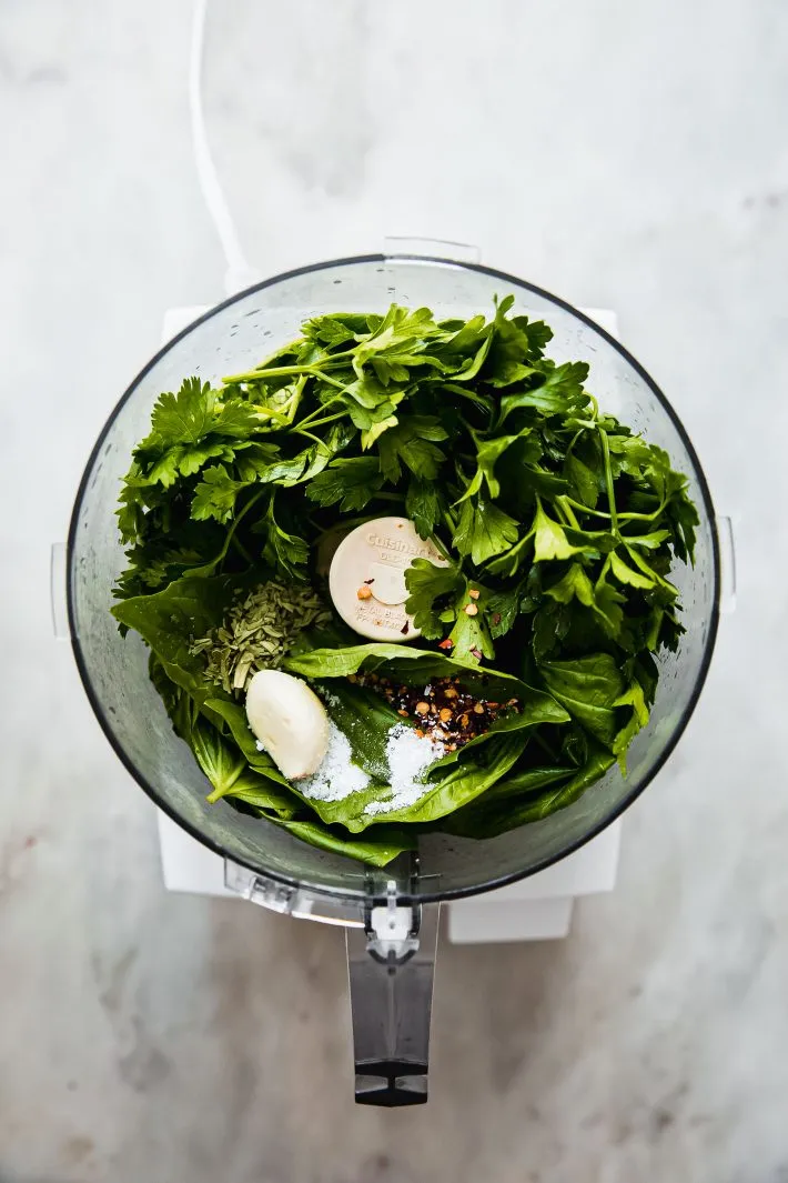 Ingredients including fresh parsley, cilantro, garlic, and oil in a food processor, ready to blend into a garden herb vinaigrette