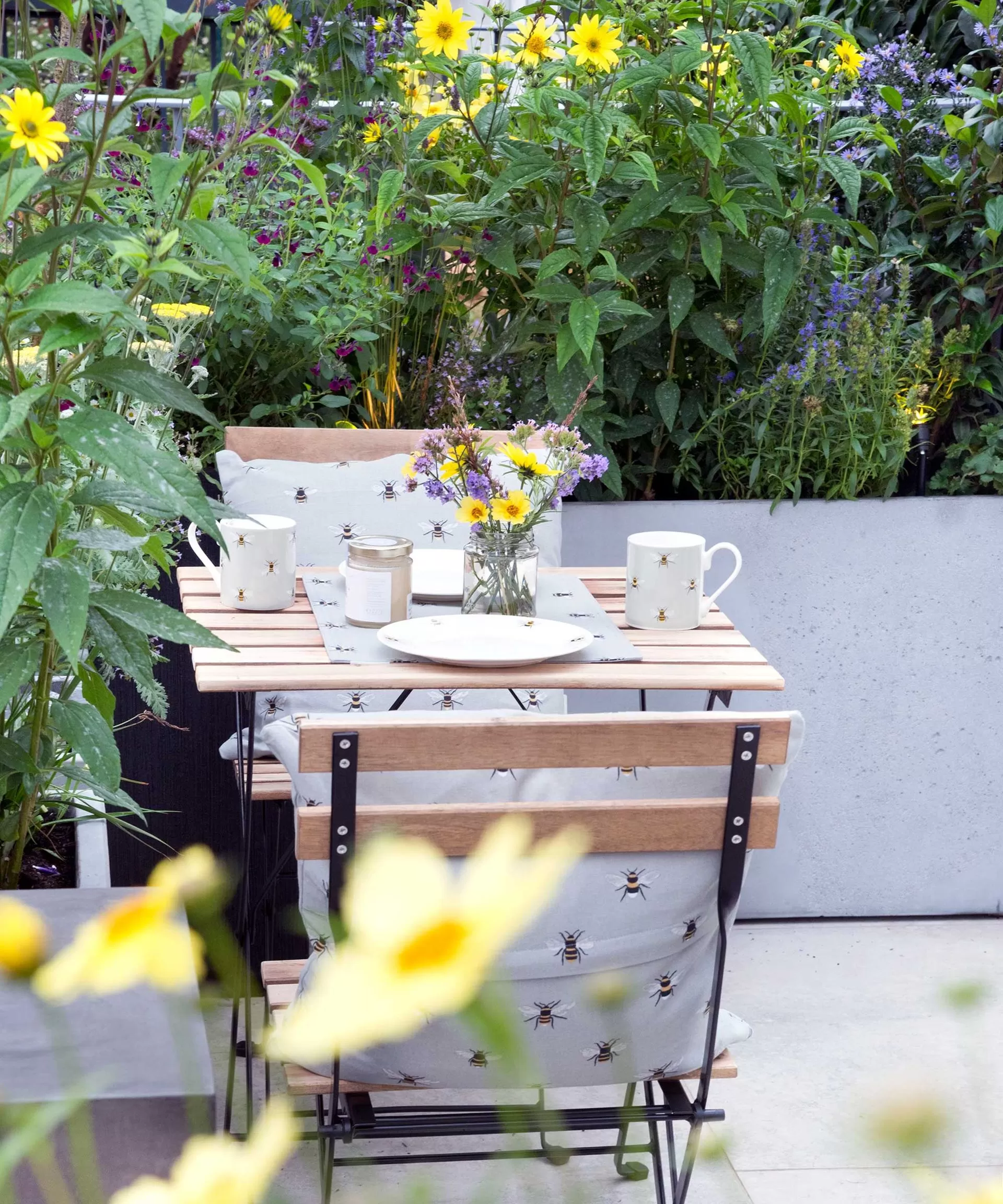 Shaded balcony garden featuring lush green plants in various pots and containers surrounding a small bistro table and chairs, creating a relaxing urban retreat perfect for planting shade-loving perennials in balcony pots.