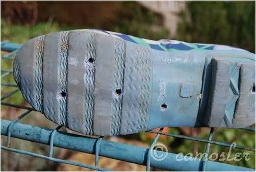 A person drills drainage holes into the sole of a vibrant red wellington boot