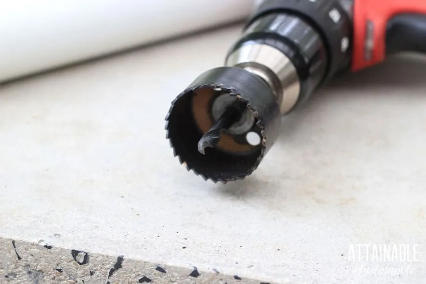 A hole saw drill bit attached to a power drill, ready for cutting planting pockets in a PVC pipe.